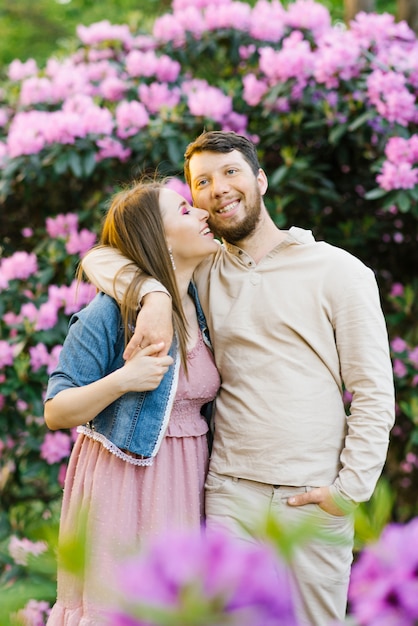 Happy smiling young couple. They embrace and rest in the spring in a blooming garden of rhododendrons