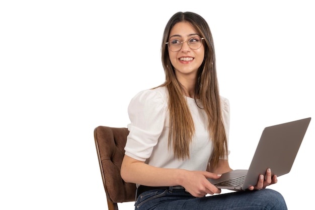 Happy smiling young girl working on laptop Sitting on the chair isolated over white background