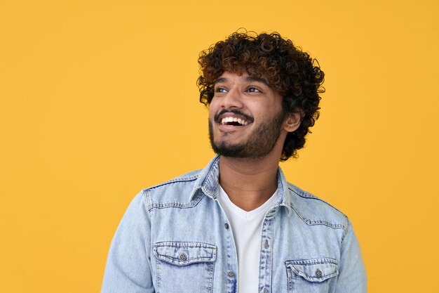 Photo happy smiling young indian man looking dreaming on yellow background