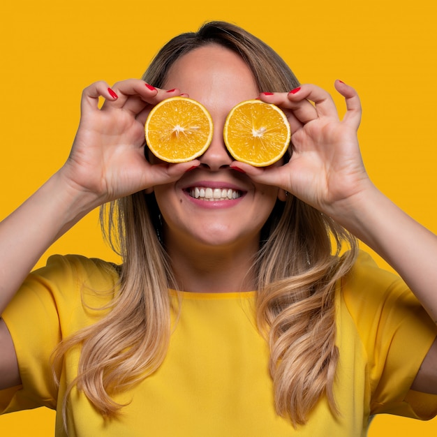 Happy and smiling young man playing with an orange cut in half and in front of his eyes. 