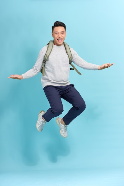 счастливый улыбающийся молодой человек с рюкзаком прыгает