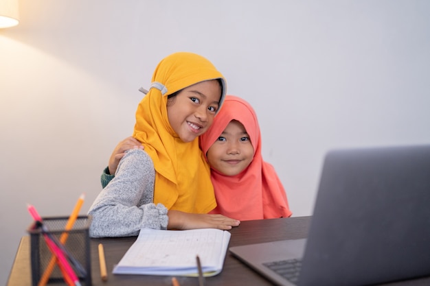 Happy smiling young muslim kid with laptop together looking at camera