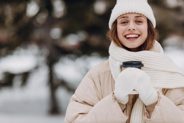 幸せな笑顔の若い女性の肖像画 衣装のコート スカーフ 帽子と手袋 雪の冬の公園で冬の天気を楽しんでいます