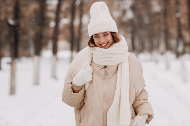 Happy smiling young woman portrait dressed coat scarf hat and mittens enjoys winter weather at snowy winter park