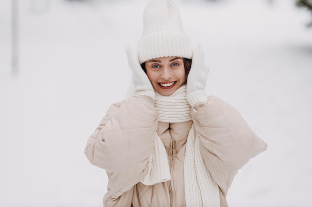 幸せな笑顔の若い女性がスカーフの帽子と手袋をかぶって ⁇ 雪の冬の公園で冬の天気を楽しんでいます ⁇ 