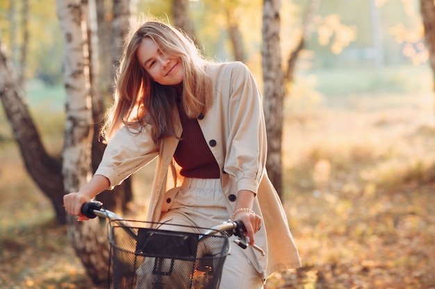 Happy smiling young woman riding vintage bicycle in autumn park at sunset