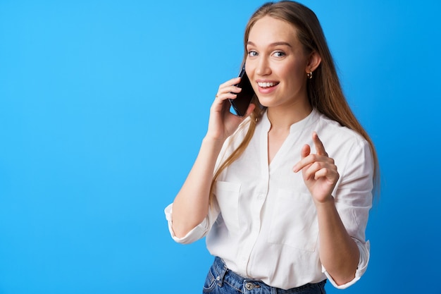 Happy smiling young woman talking on the phone against blue background