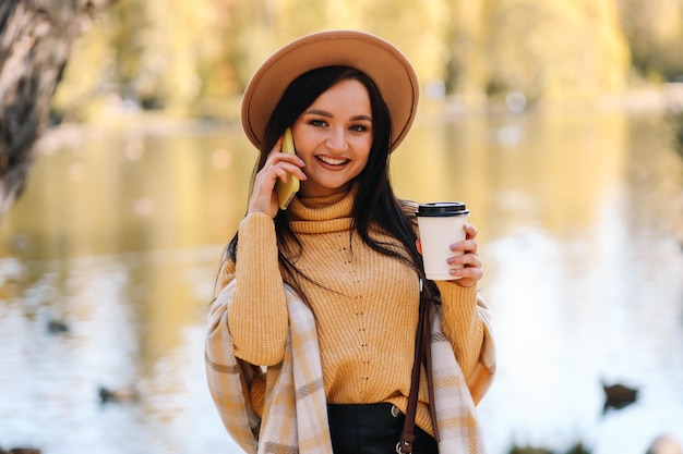 A happy smiling young woman in warm clothes walks in an autumn park in nature in fall