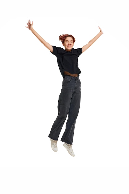 Photo happy smiling young woman wearing casual black cloth raised hands while jumping on white studio