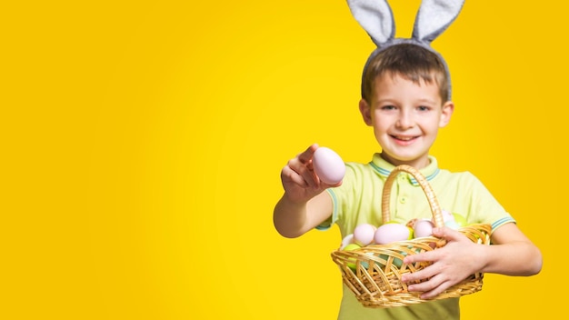 A happy smilling boy with easter bunny ears holds a basket with painted eggs