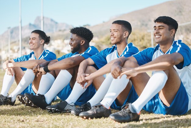 Happy soccer players relax or team on a field for a sports game together in summer on resting break Smile stadium or group of football athletes sitting after fitness exercise training or match