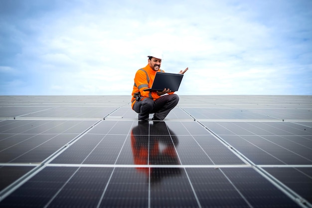 Happy solar panel worker using laptop and checking electricity production in sustainable power plant