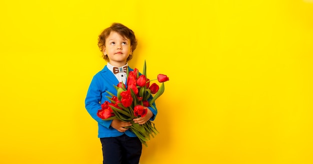 A happy son, a boy in a blue jacket and a butterfly holds a huge bouquet of red tulips