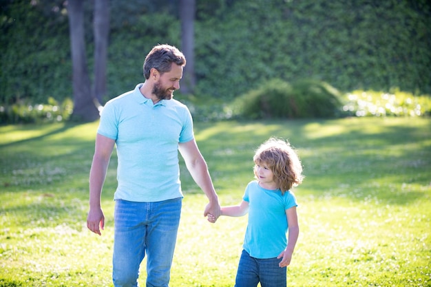 Happy son and father holding hands walking on sunny summer day in park grass fatherhood