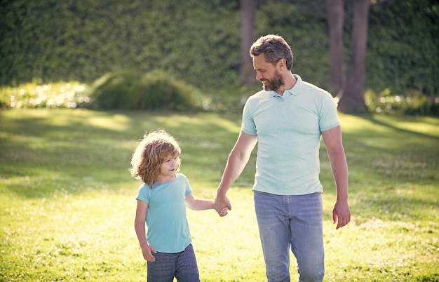 Happy son and father holding hands walking on sunny summer day in park grass fatherhood