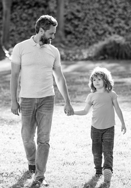 Happy son and father holding hands walking on sunny summer day in park grass togetherness