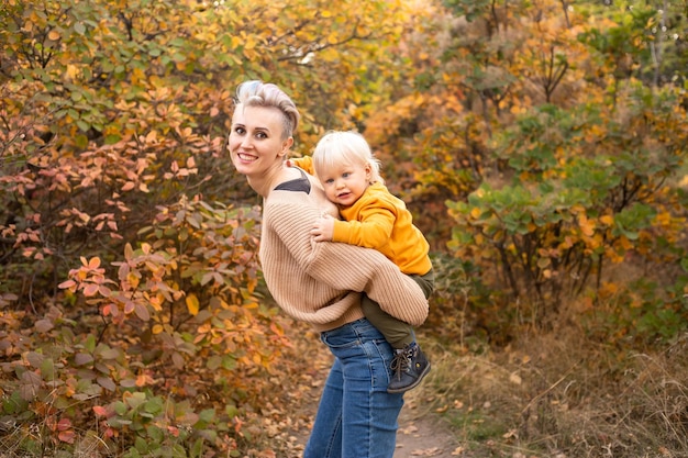 Happy son with mother in autumn park background with golden trees