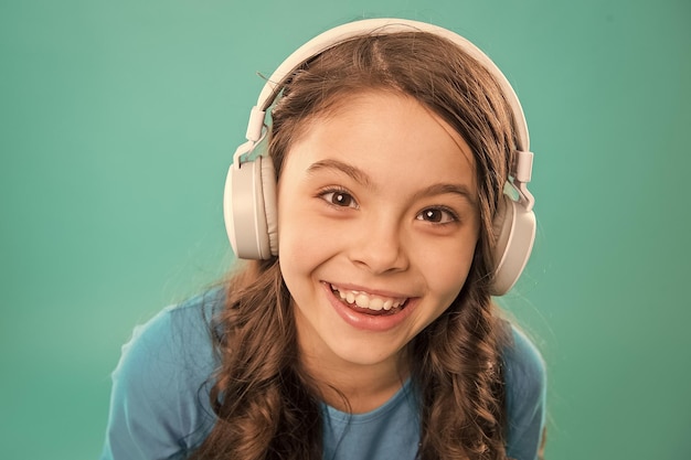 Happy songs to make you smile Happy small girl listening to music on blue background Little child enjoying song playing in headphones with smile on happy face Happy fun and upbeat