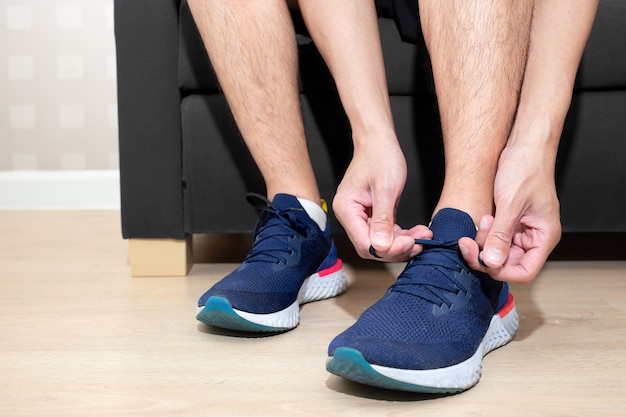 Happy sport man tie shoelace of his running shoe on sofa in home living room for running