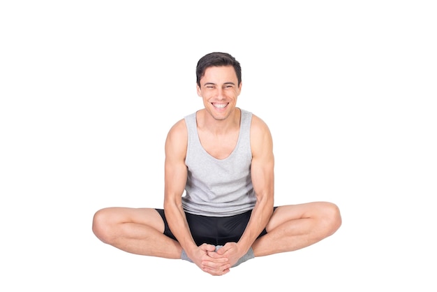 Foto uomo sportivo felice in abbigliamento sportivo che guarda la fotocamera con un sorriso mentre allunga i muscoli adduttori isolati su sfondo bianco in studio