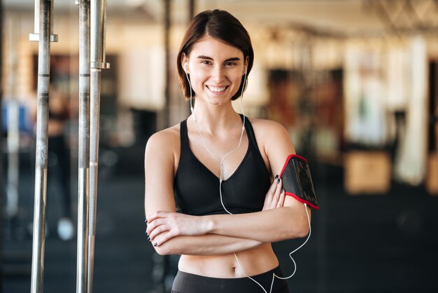 Happy sportswoman with armband listening to music in gym