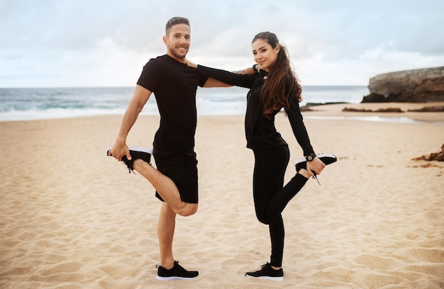 Happy sporty couple doing stretching for legs warming up before training on ocean beach looking and