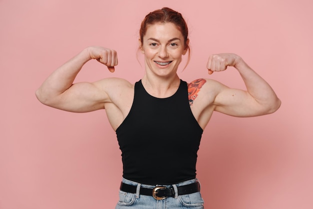 Photo happy sporty muscular woman with red hair in tshirt and jeans smiling with braces and showing biceps