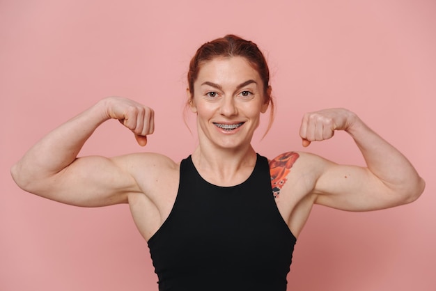 Photo happy sporty muscular woman with red hair in tshirt and jeans smiling with braces and showing biceps