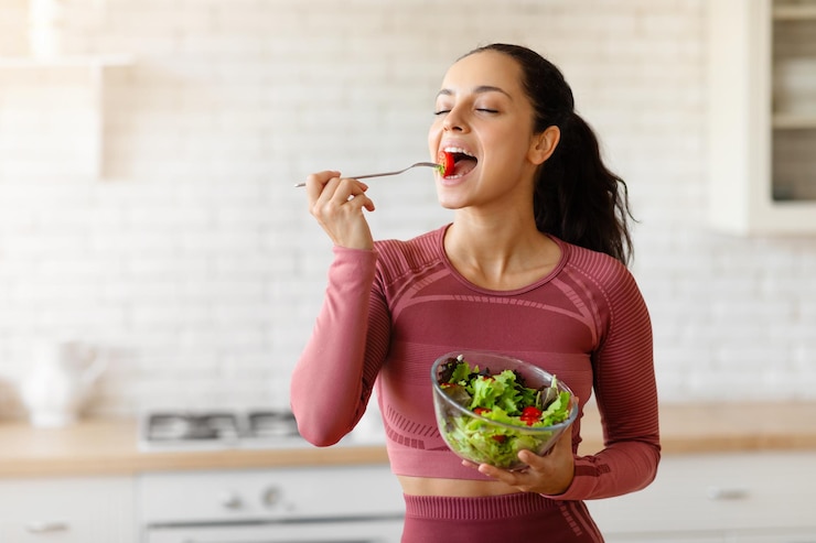 Photo happy sporty woman eats fresh salad in the kitchen indoor