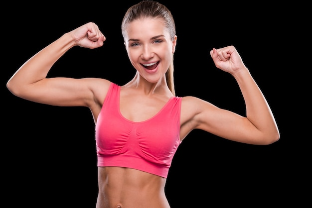 Happy sporty woman. Happy young and sporty woman exercising with dumbbells and smiling while standing against black background