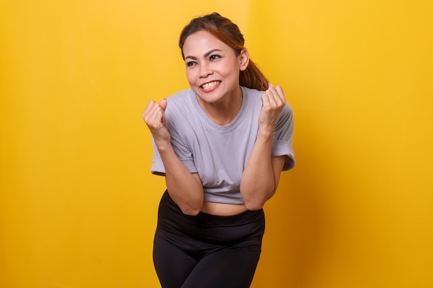 Happy sporty woman in sportswear celebrating win and success over yellow background