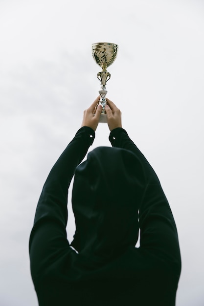 Happy sporty young woman holding gold trophy cup