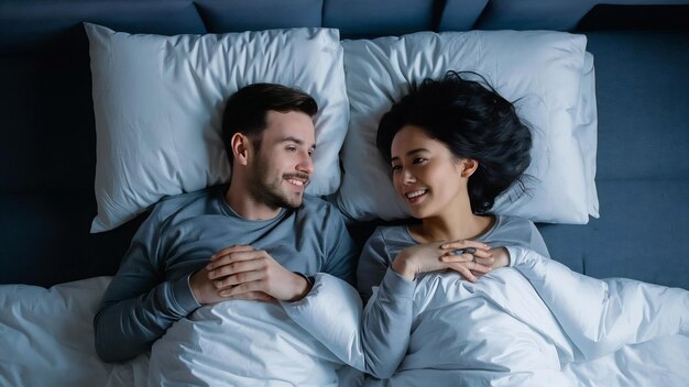 Happy spouses enjoy spending time together lie under white blanket have positive expressions and