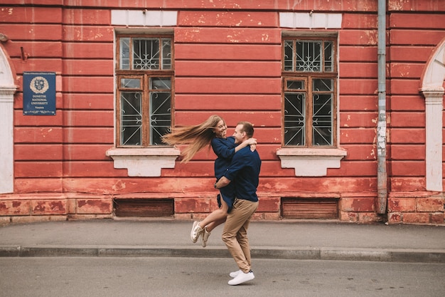 The happy state of a young couple against the background of a red wall, the girl jumped on the guy