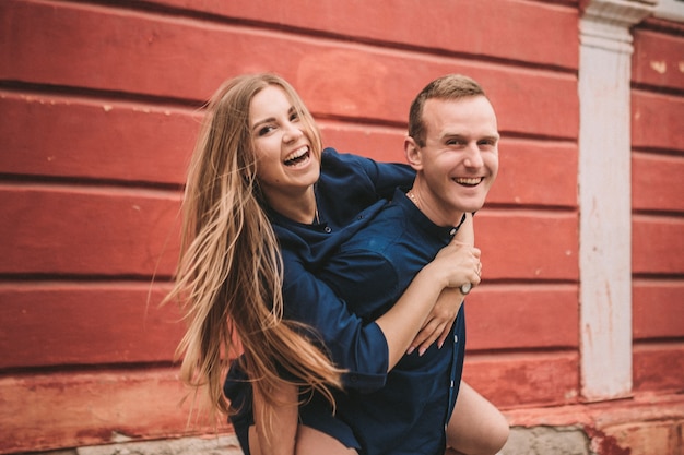 The happy state of a young couple against the background of a red wall, the girl jumped on the guy