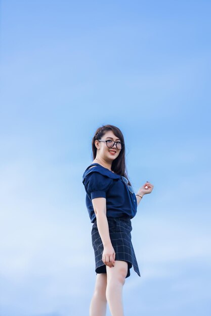Happy Stretching Relaxation Resting Portrait asian woman Wear dark blue dress stand on bright blue sky background at the city park outdoors