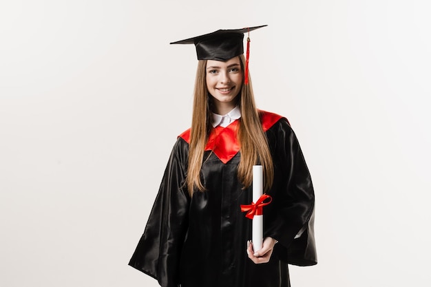 Happy student in black graduation gown and cap is smiling on white background Graduate girl is graduating high school and celebrating academic achievement Masters degree diploma in hands