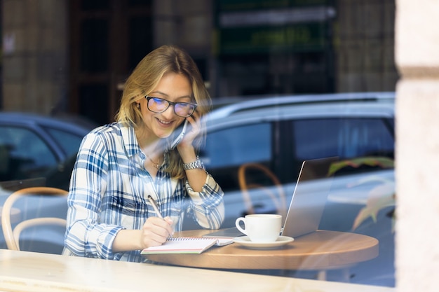 Happy student in a cafe talking on the mobile phone