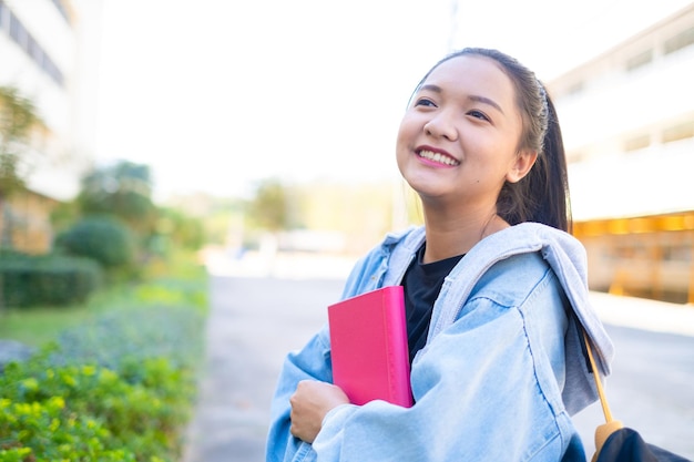 幸せな学生の女の子は学校で本とバックパックを持っています、アジアの女の子。