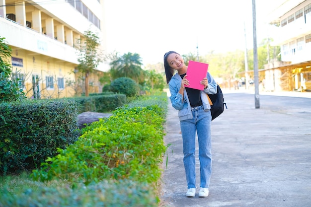 幸せな学生の女の子は学校で本とバックパックを保持しますアジアの女の子