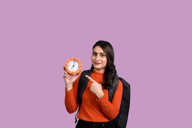 Happy student girl holding an alarm clock pointing with finger indian pakistani model