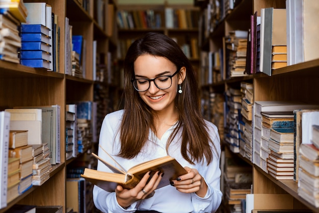 図書館で幸せな学生の女の子。大学の図書館の文学部で小説を読む魅力的な白人女子学生