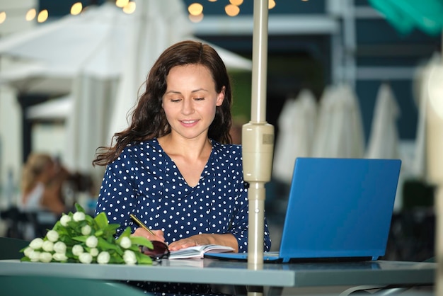 Happy student girl studying remotely on laptop computer while sitting at outdoor cafe table Concept of taking university courses online