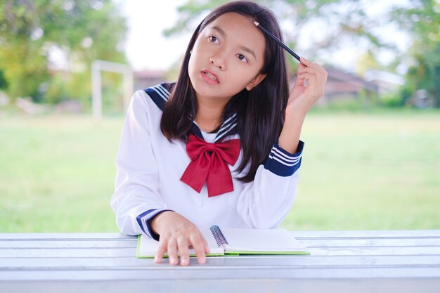 学校の戸外に座っている本を持つ幸せな学生の女の子アジアの女の子