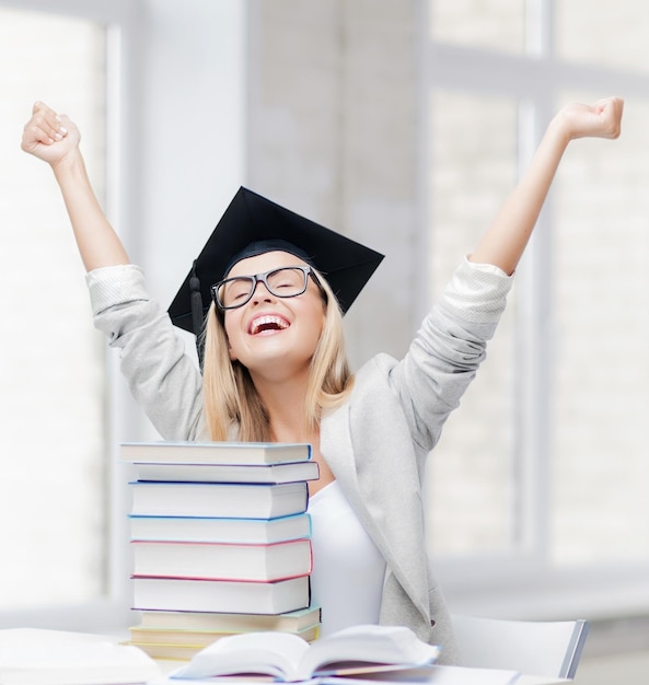 Foto studente felice in berretto di laurea con pila di libri