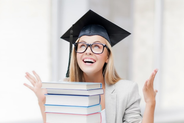 счастливый студент в выпускной шапке со стопкой книг