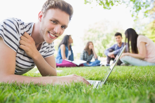 Happy student using his laptop outside at the university