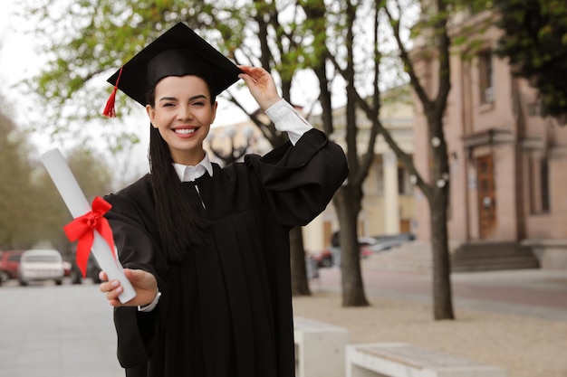 Happy student with diploma after graduation ceremony outdoors Space for text