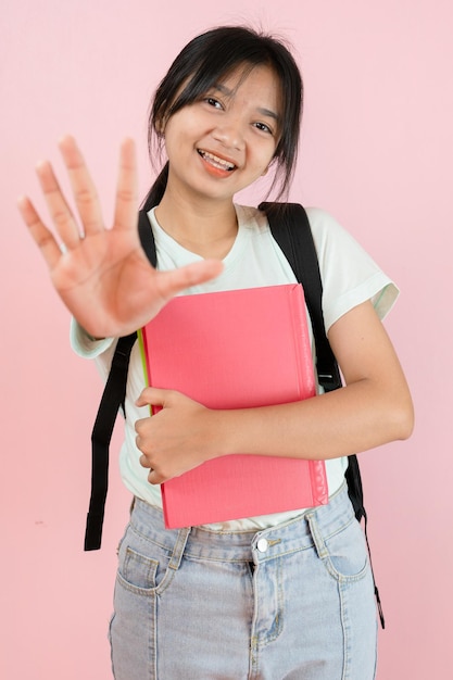 幸せな学生の若い女の子は、ピンクの背景にピンクの本とバックパックを保持します。