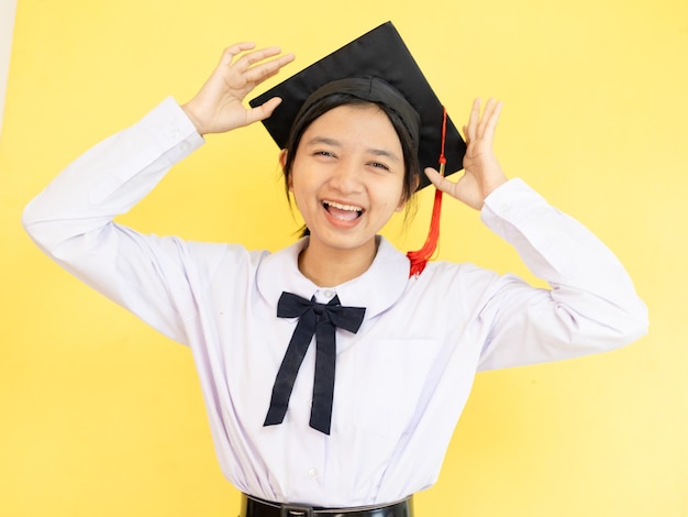 Счастливая студентка носит выпускную шляпу на желтом фоне.